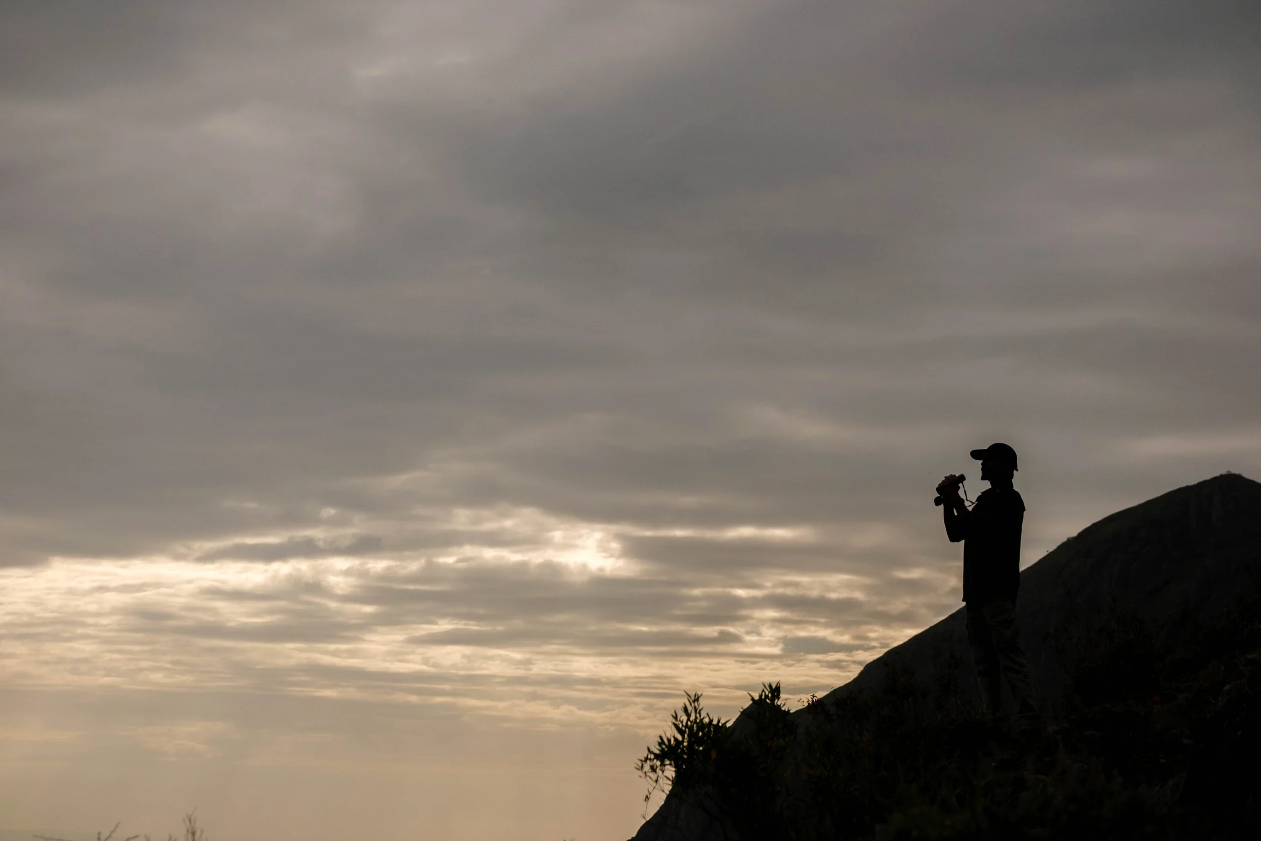 A birdwatcher silhouetted on the mountainside under a dusky sky