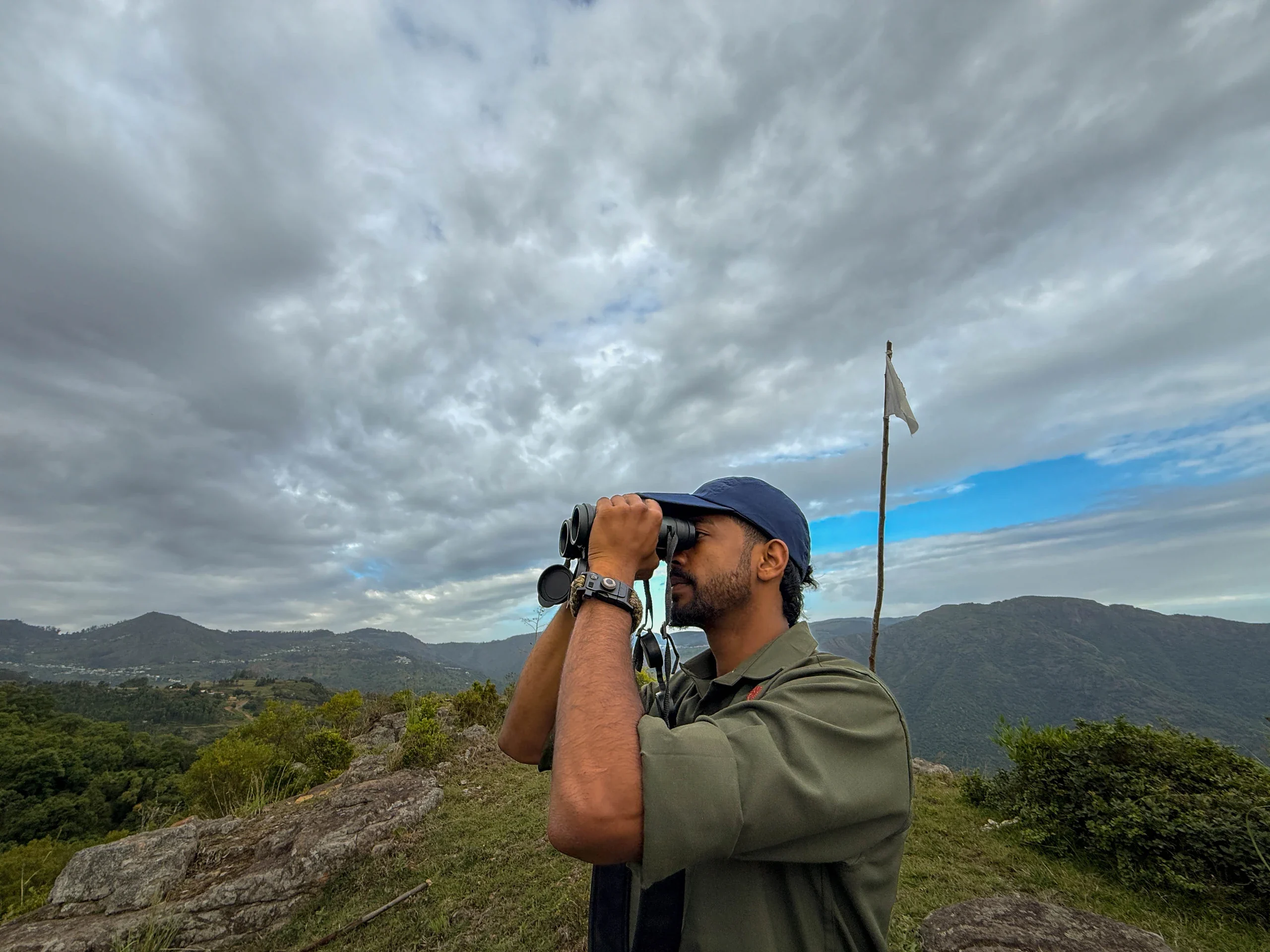 A birdwatcher looking through binoculars on a rocky highland ridge