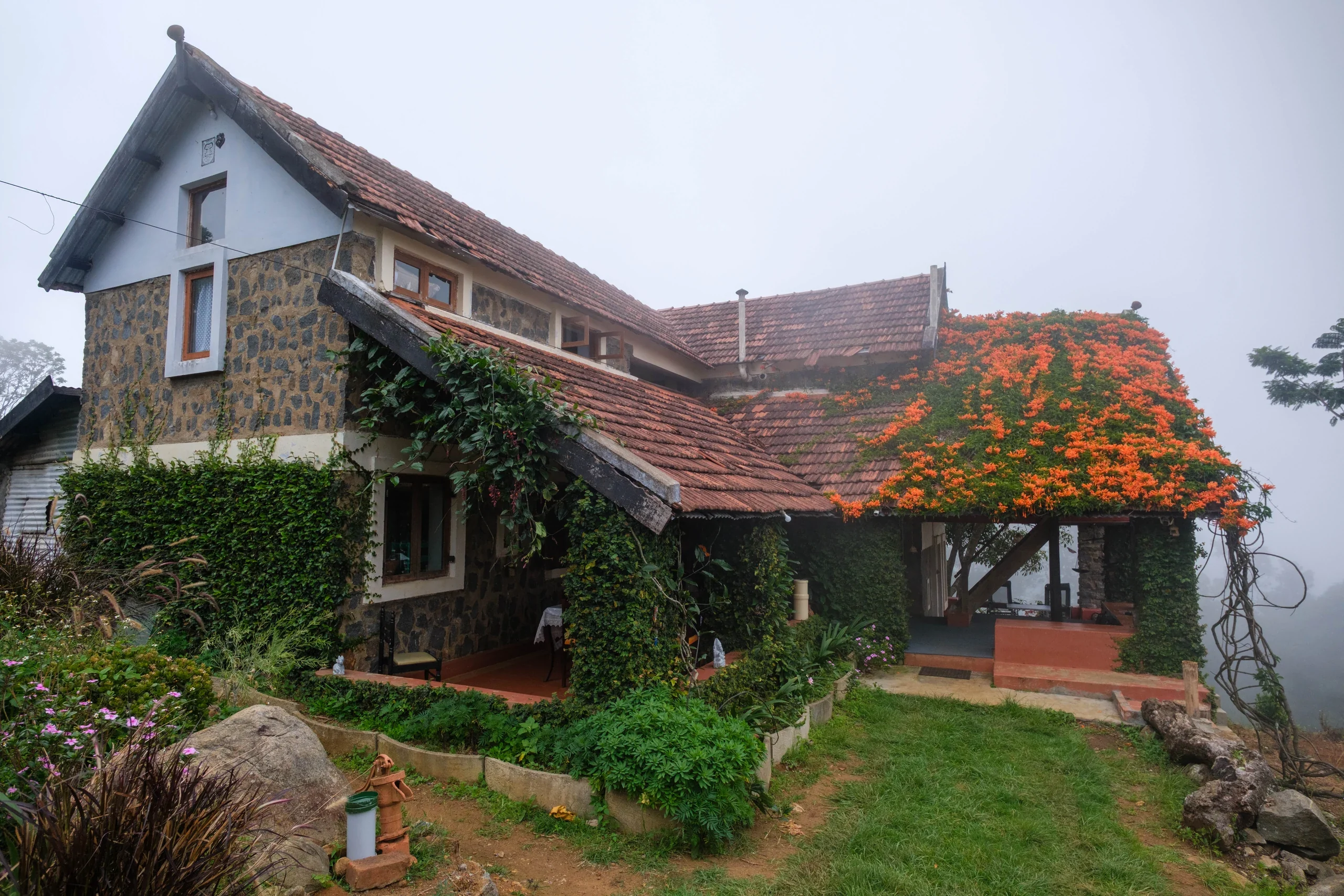 Hullathy stone bungalow framed by flowering vines and Nilgiri mountain mist
