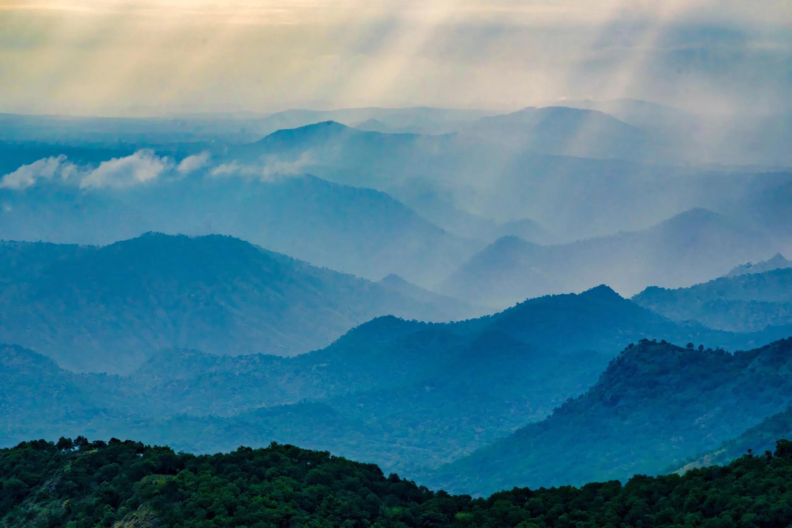 Shafts of sunlight falling across layered blue mountain ridges